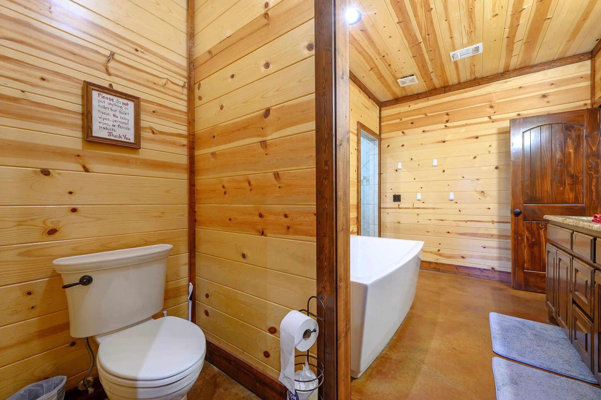 A wooden cabin bathroom with a toilet, sink, and shower.