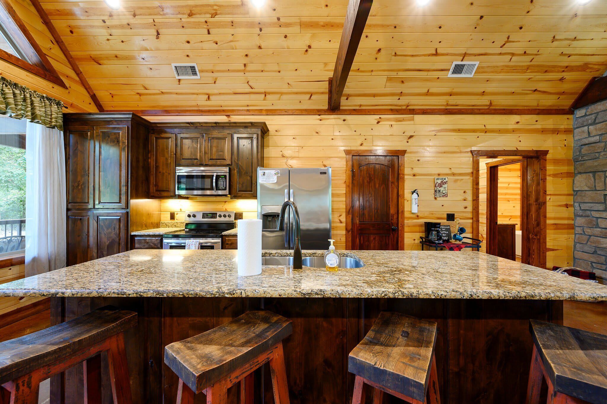 Una cocina con paredes de madera, encimeras de granito y una isla central con taburetes de bar.
