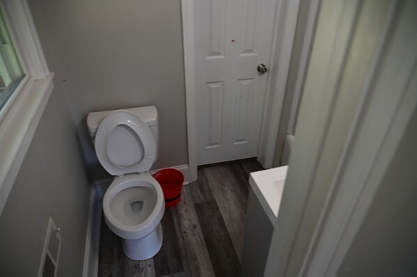 Un baño pequeño con un inodoro, un cubo rojo y una puerta blanca.