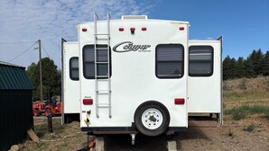 A white RV with a ladder on the back, parked on gravel. - Cool RV with AC in Bayfield next to small lake (Bayfield)