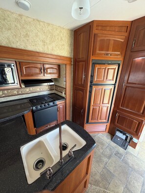 A kitchen with wooden cabinets, a black stove, and a double sink. - Cool RV with AC in Bayfield next to small lake (Bayfield)