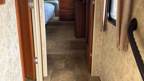 A narrow hallway with a bed and a small kitchenette in the background. - Cool RV with AC in Bayfield next to small lake (Bayfield)