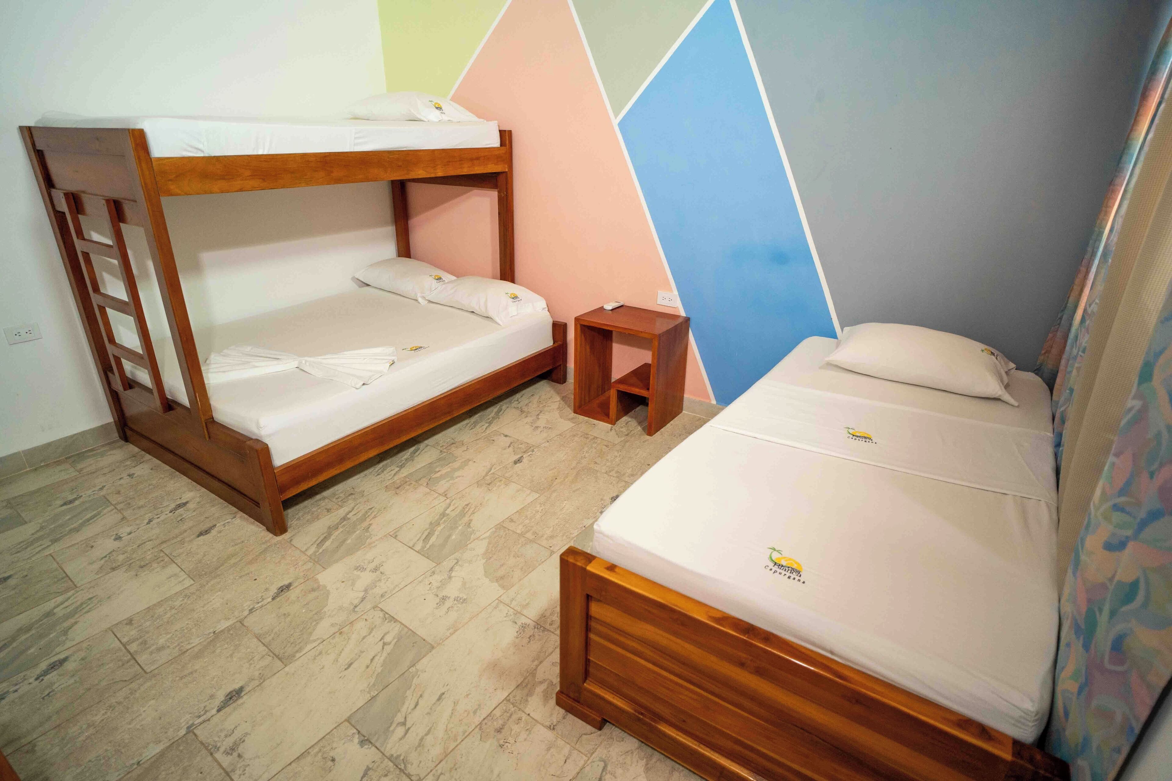 Una habitación con dos literas, una mesita de noche de madera y un diseño de pared geométrico y colorido.