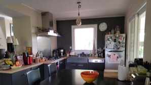 A modern kitchen with a central island, black chairs, a large orange bowl, and a clock on the wall. - Villa ardéchoise 150m2 with swimming pool Available from August 23 to 30 1850€/sem (ST DIDIER SOUS AUBENAS)