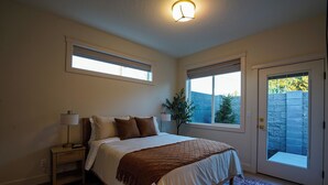A bedroom with a bed, bedside table, lamp, and two windows. - Brand new 2-bedroom home in the heart of Kennewick (Kennewick)