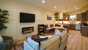 A modern living room with a fireplace, a flat-screen TV, a sofa, and a dining area. - Brand new 2-bedroom home in the heart of Kennewick (Kennewick)