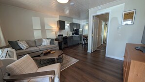 Un salon comprenant un canapé, une table basse et un fauteuil. Il y a également un coin cuisine avec des placards et une cuisinière.