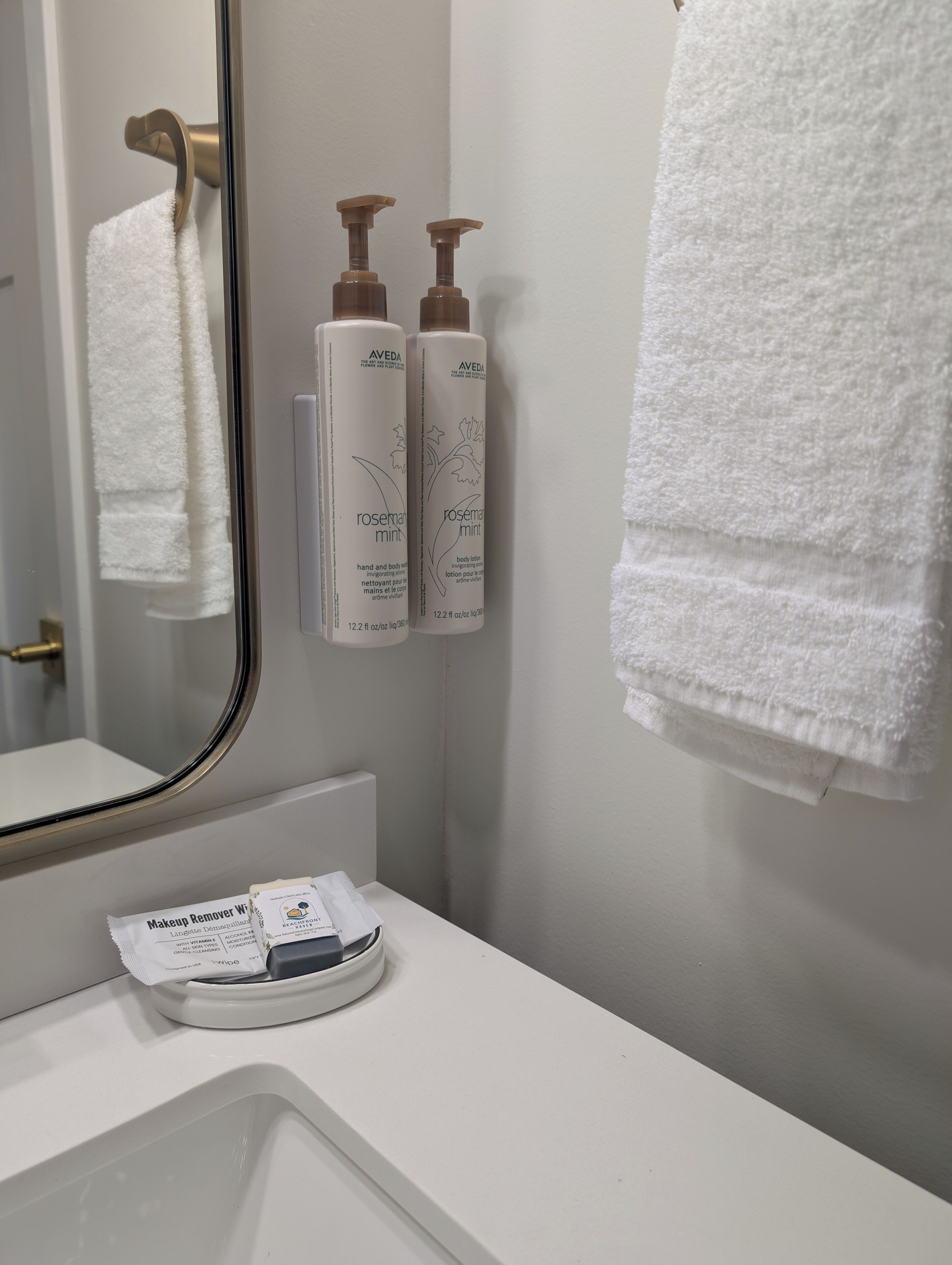 A bathroom with a white sink, a mirror, and two bottles of Aveda body lotion.