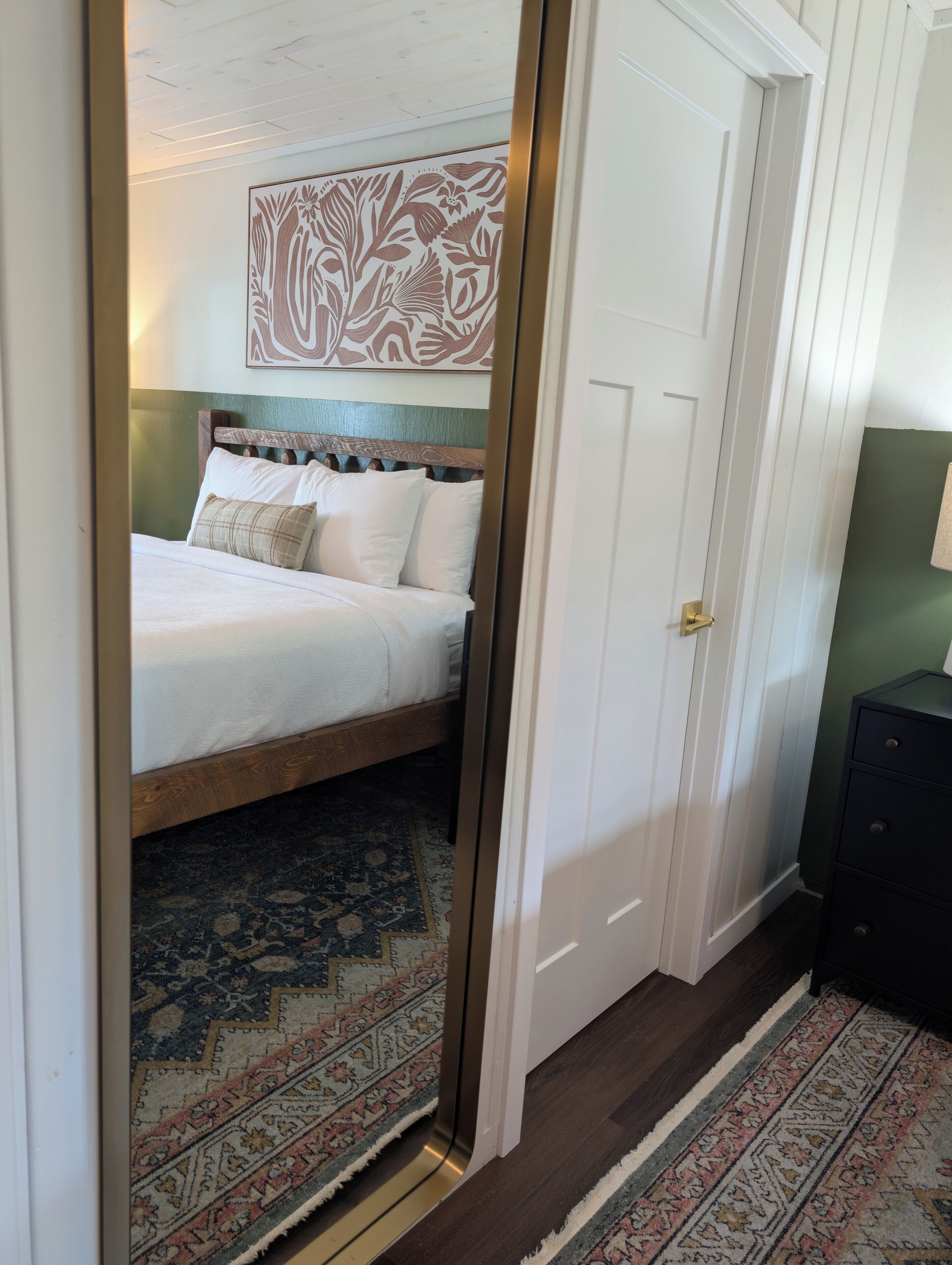 Quarto com cama, tapete estampado, cabeceira de madeira e uma porta.