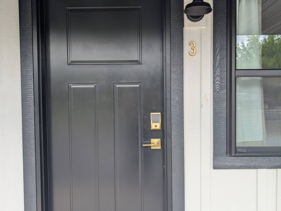 A black front door with a keypad lock, a small window with a number '3' above it, and a black doormat at the entrance.