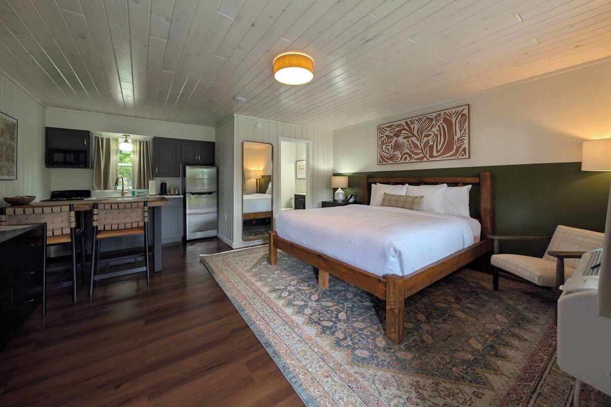 A bedroom with a large bed, a wooden headboard, a nightstand, a lamp, and a mirror.