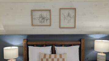 A neatly made bed with two pillows and two bedside tables with lamps. There are two framed artworks on the wall above the bed.