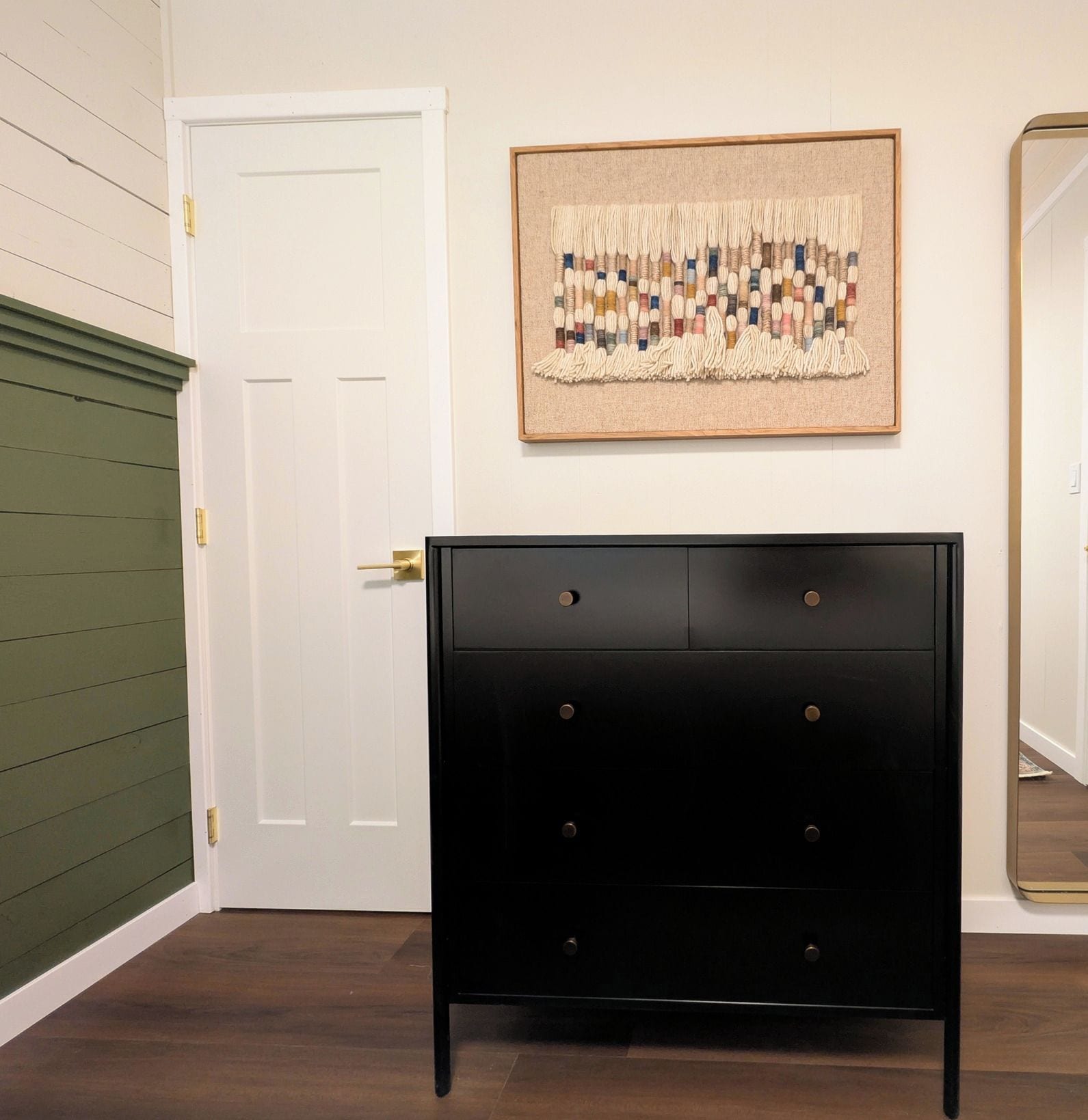 Um quarto com cômoda preta, uma obra de arte emoldurada na parede e um espelho com moldura dourada.