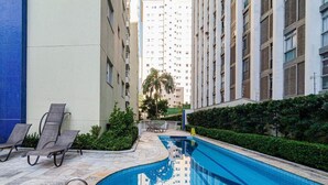 A swimming pool with lounge chairs, surrounded by tall residential buildings and greenery.