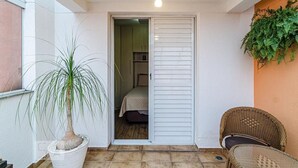 A small, private room with a bed, a potted plant, and a wicker chair.
