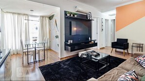 A modern living room with a flat-screen TV mounted on the wall, a glass dining table, and a black coffee table.