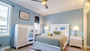 A bedroom with a bed, two nightstands, a dresser, a ceiling fan, and a window.