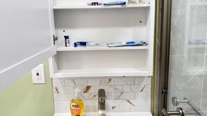 A bathroom with a white vanity, a mirror, a sink, and a shower area.