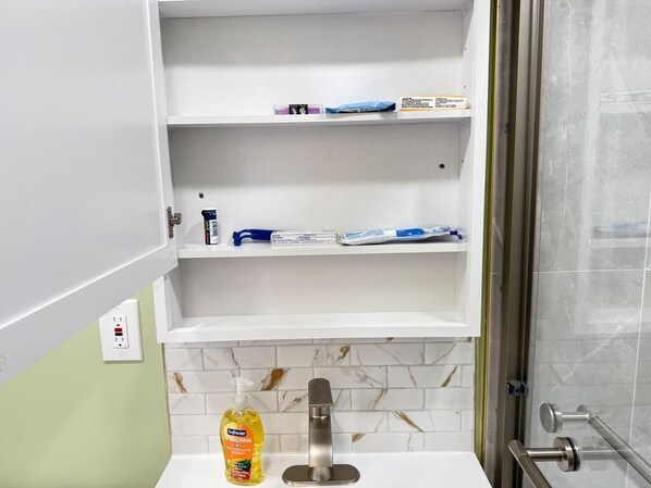 A bathroom with a white vanity, a mirror, a sink, and a shower area.