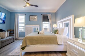 A bedroom with a bed, a dresser, a nightstand, a ceiling fan, and a window with curtains.