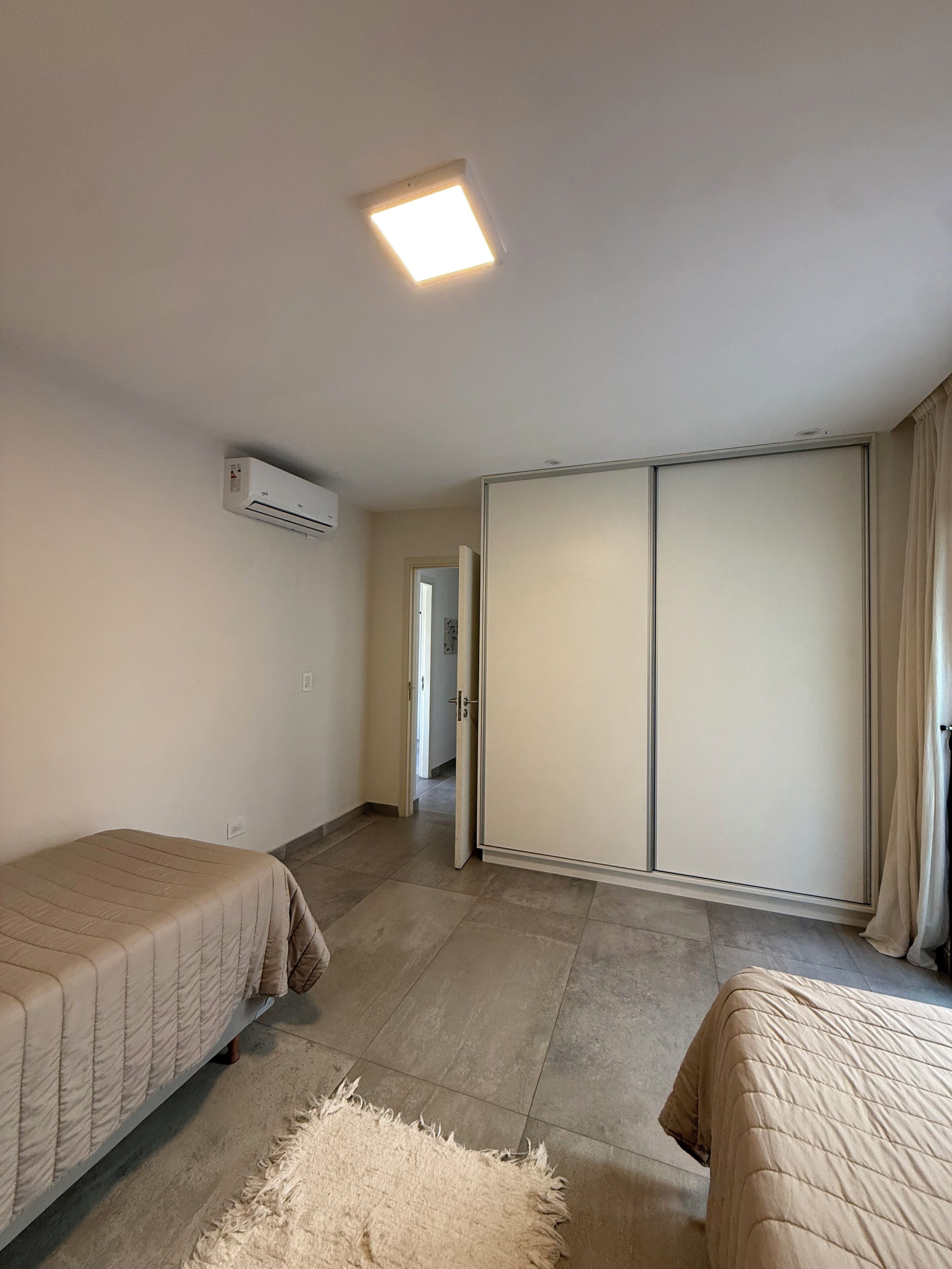 A bedroom with two beds, a wardrobe, an air conditioning unit, and a light fixture.