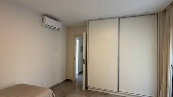 A bedroom with two beds, a wardrobe, an air conditioning unit, and a light fixture.