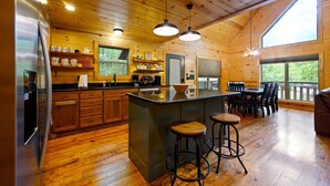 Una cocina amplia con armarios de madera, una isla central con taburetes y ventanas grandes con vistas al exterior.
