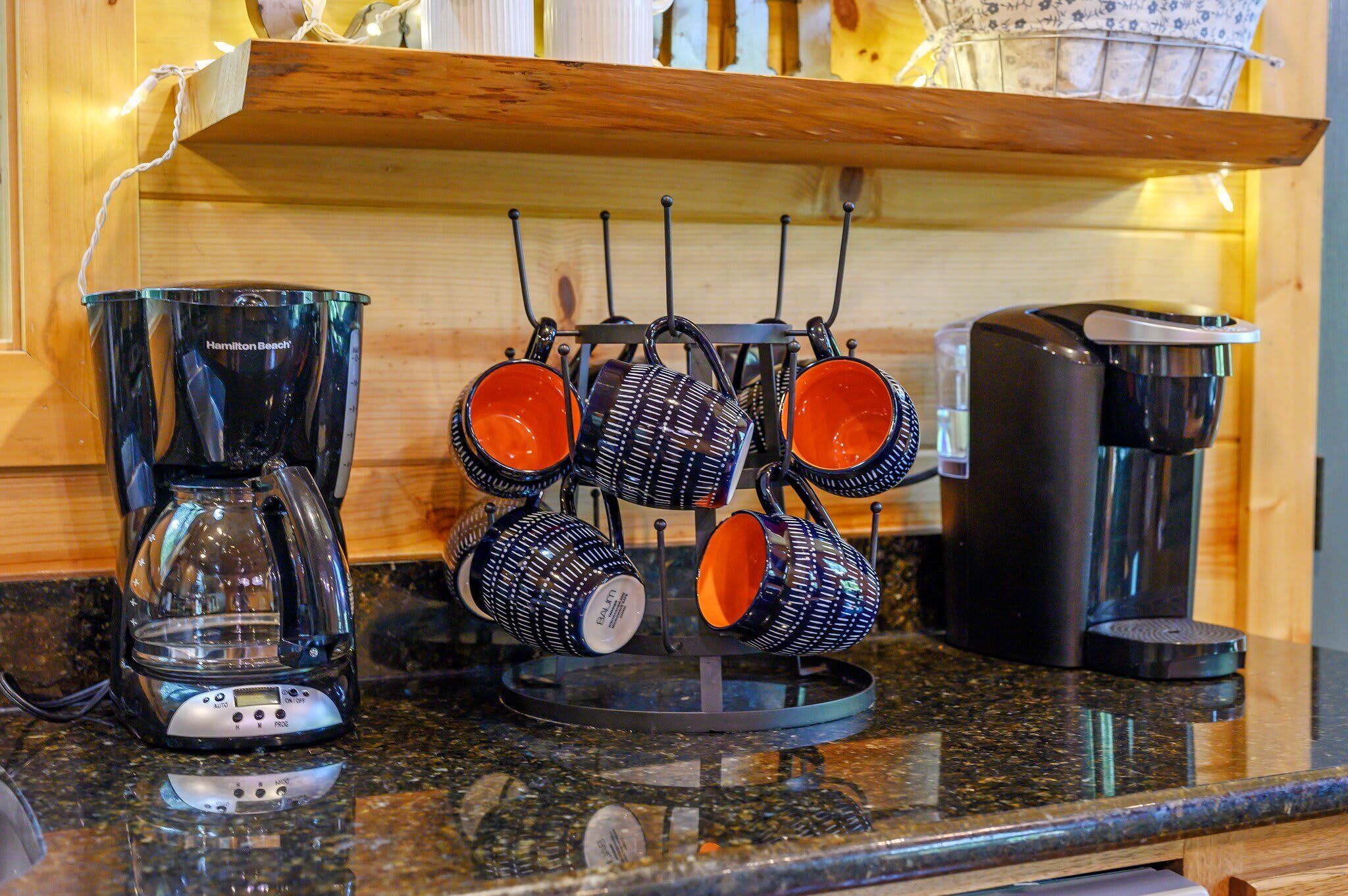 A kitchen counter with a coffee maker, a mug rack, and a coffee pot.