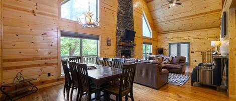 A spacious wooden cabin interior with a dining area, fireplace, and a cozy living space.