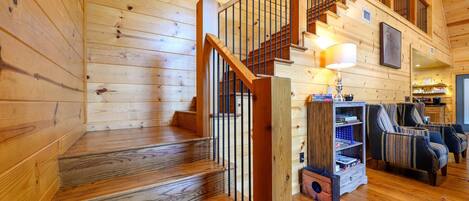 A wooden interior with a staircase, a bookshelf, and two upholstered chairs.