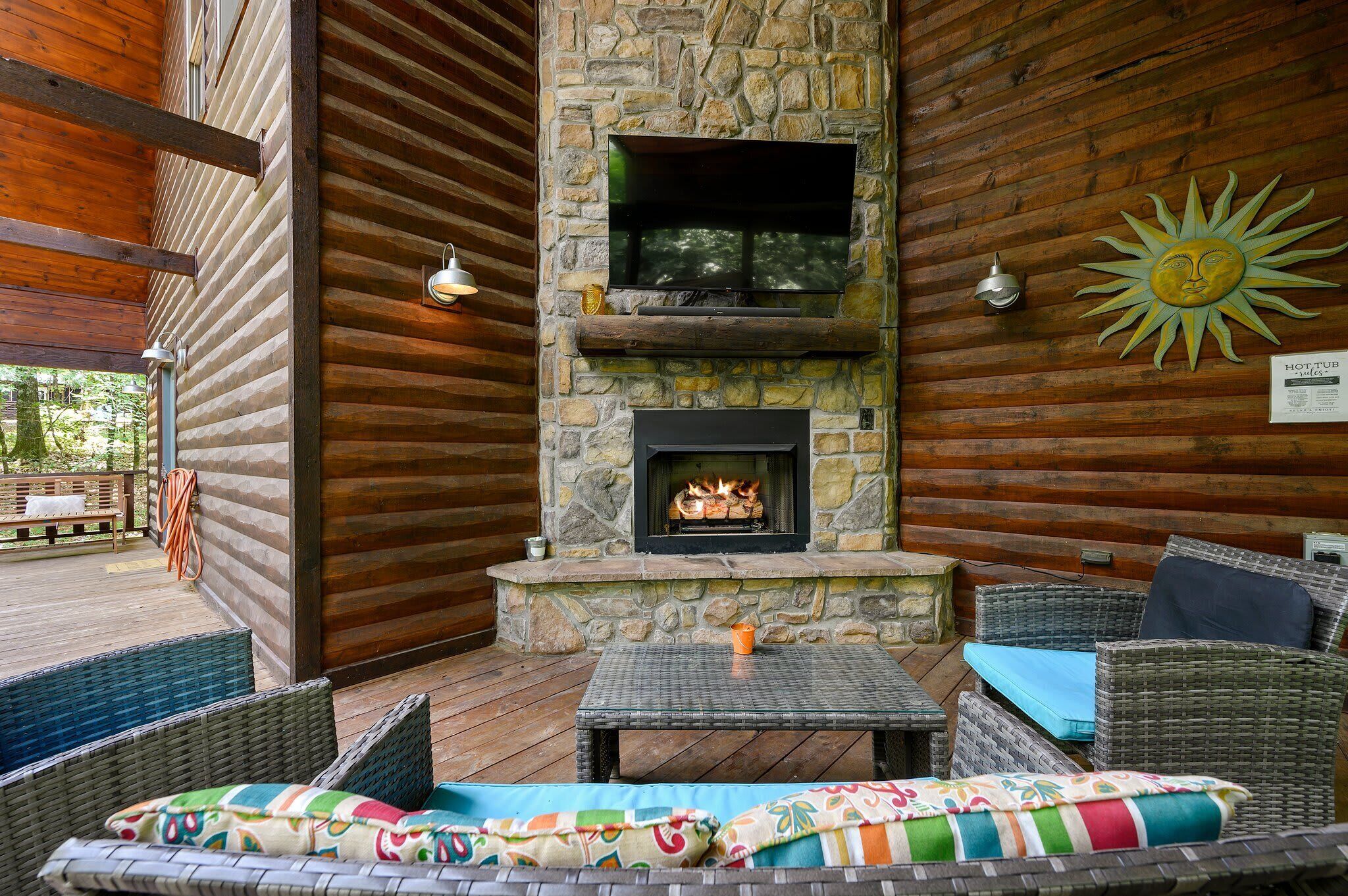 A stone fireplace with a TV above it, wicker furniture, and a sun decoration on the wall.