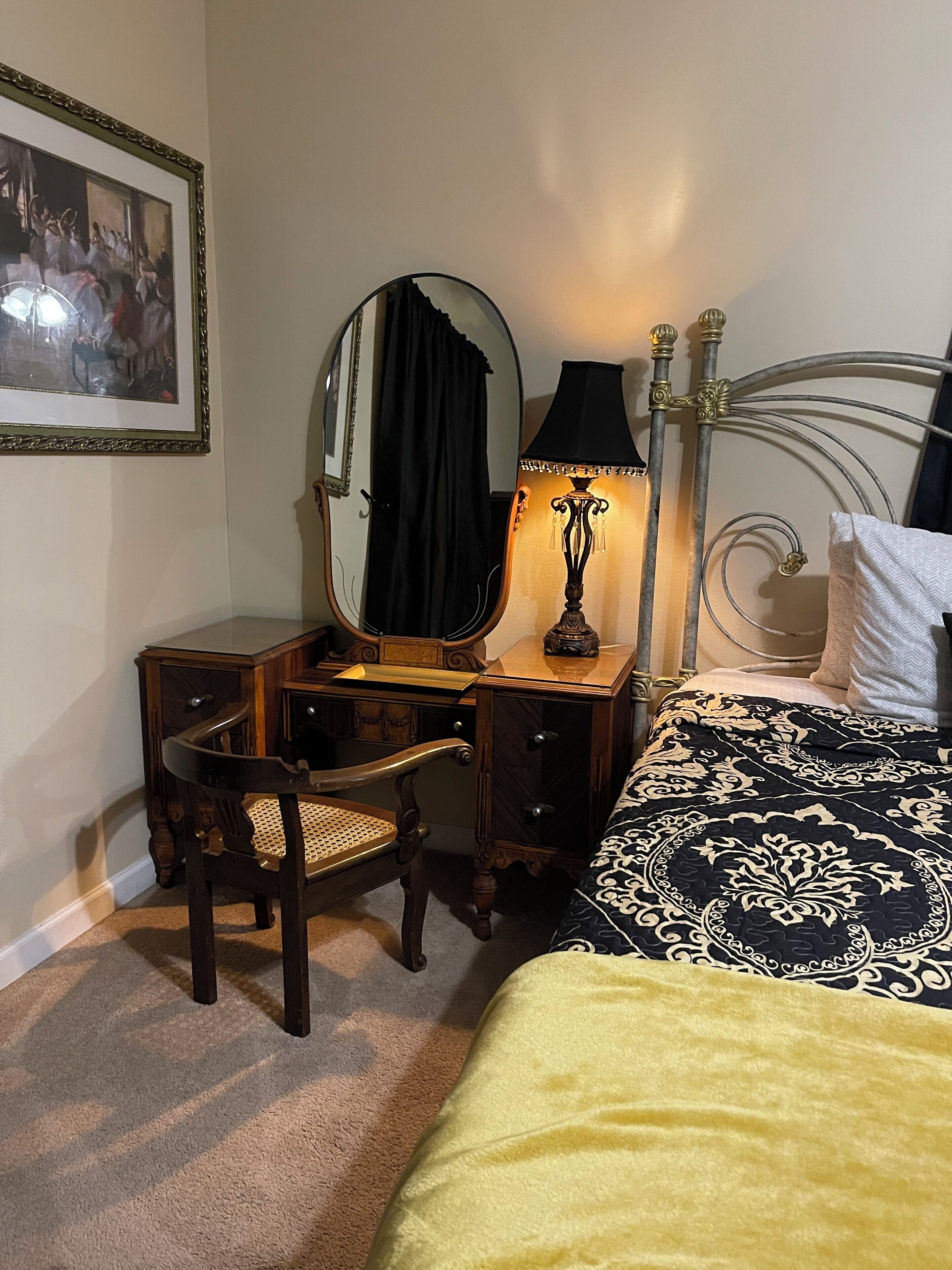 Ein Schlafzimmer mit einem Bett, einer Holzkommode, einem Sessel, einem Spiegel und einer Lampe.