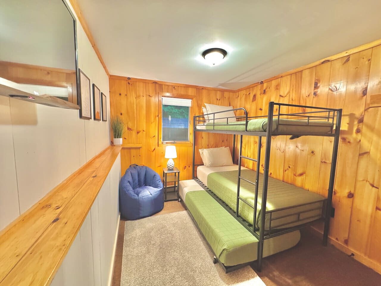 A bunk bed room with wooden walls, a small desk with a lamp, and a blue bean bag chair.