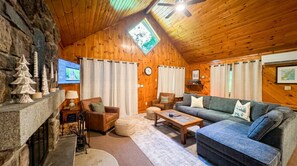 A cozy log cabin interior with a stone fireplace, wooden walls, a wooden ceiling, and a television mounted on the wall. - Rustic Luxe w/ Creek & Privacy (Bartlett)