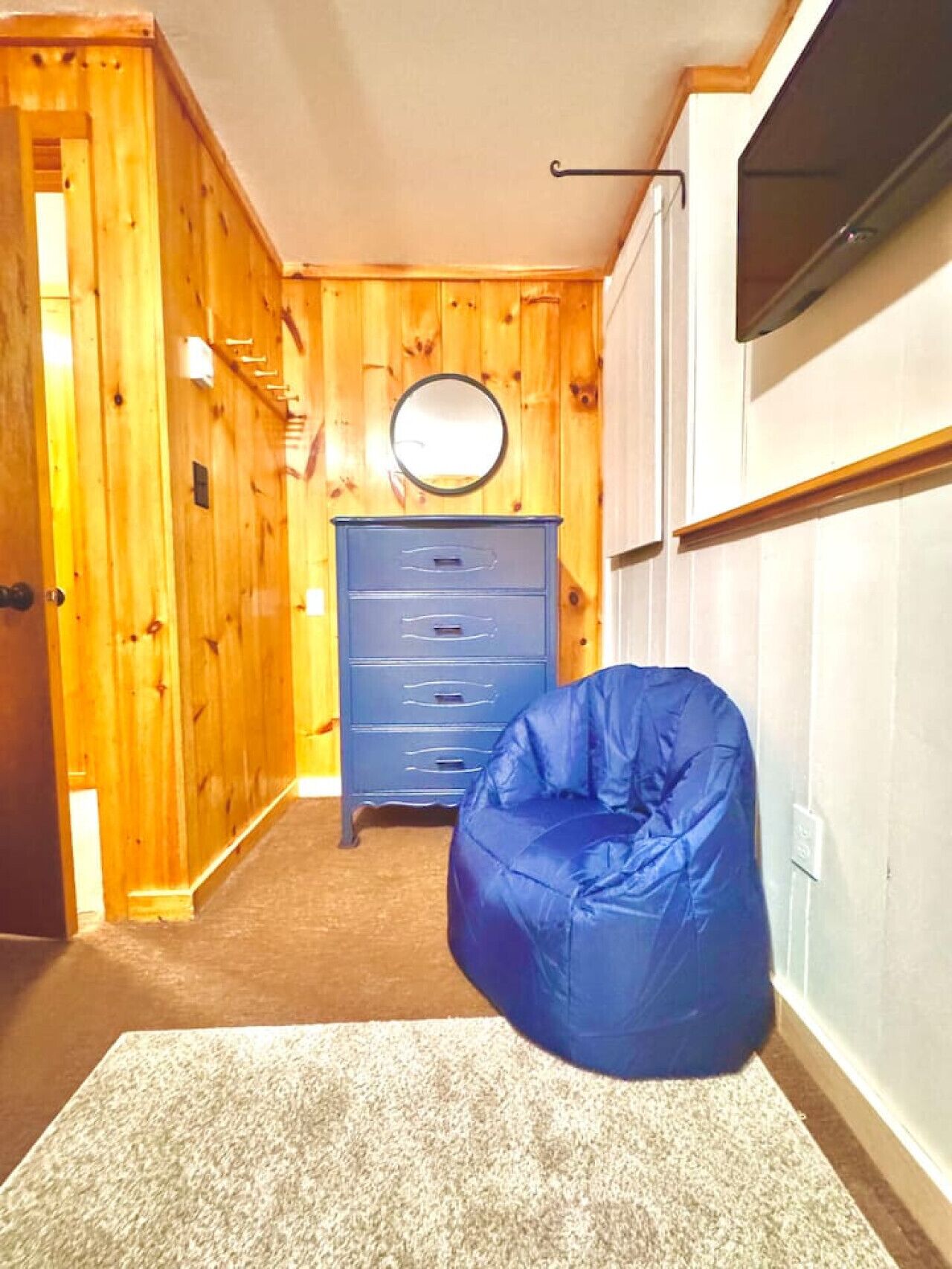 Een kamer met een houten wand, een blauwe kruisje zitzak en een dressoir met lades.