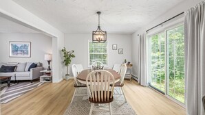 A modern dining room with a wooden table and chairs, a chandelier, and large windows with curtains. - Stylish comfort, great location (Bartlett)