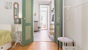 Una puerta abierta que da a un pasillo con suelo de madera, una mesita con lámpara y una silla blanca.