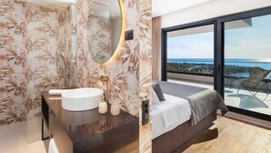 Ein modernes Badezimmer mit einem großen Spiegel, einer runden Lampe und einem Waschbecken. Das Zimmer verfügt über ein großes Fenster mit Meerblick.
