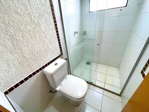A bathroom with a toilet, a shower with a glass door, and tiled walls. - Boulevard Suíte Hotel (Caldas Novas)