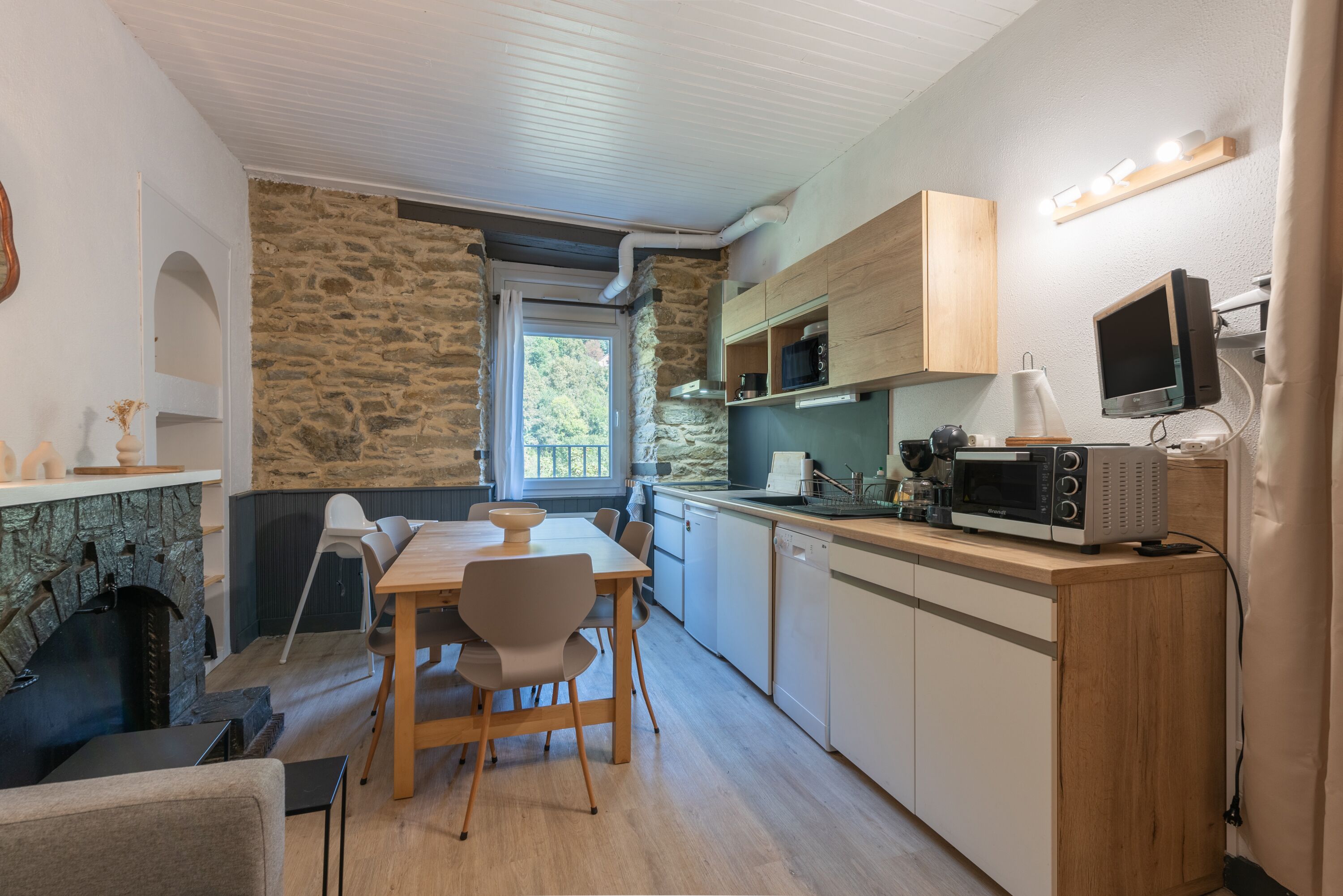 A compact kitchen with a stone wall, wooden cabinets, a dining table with chairs, and a built-in microwave.
