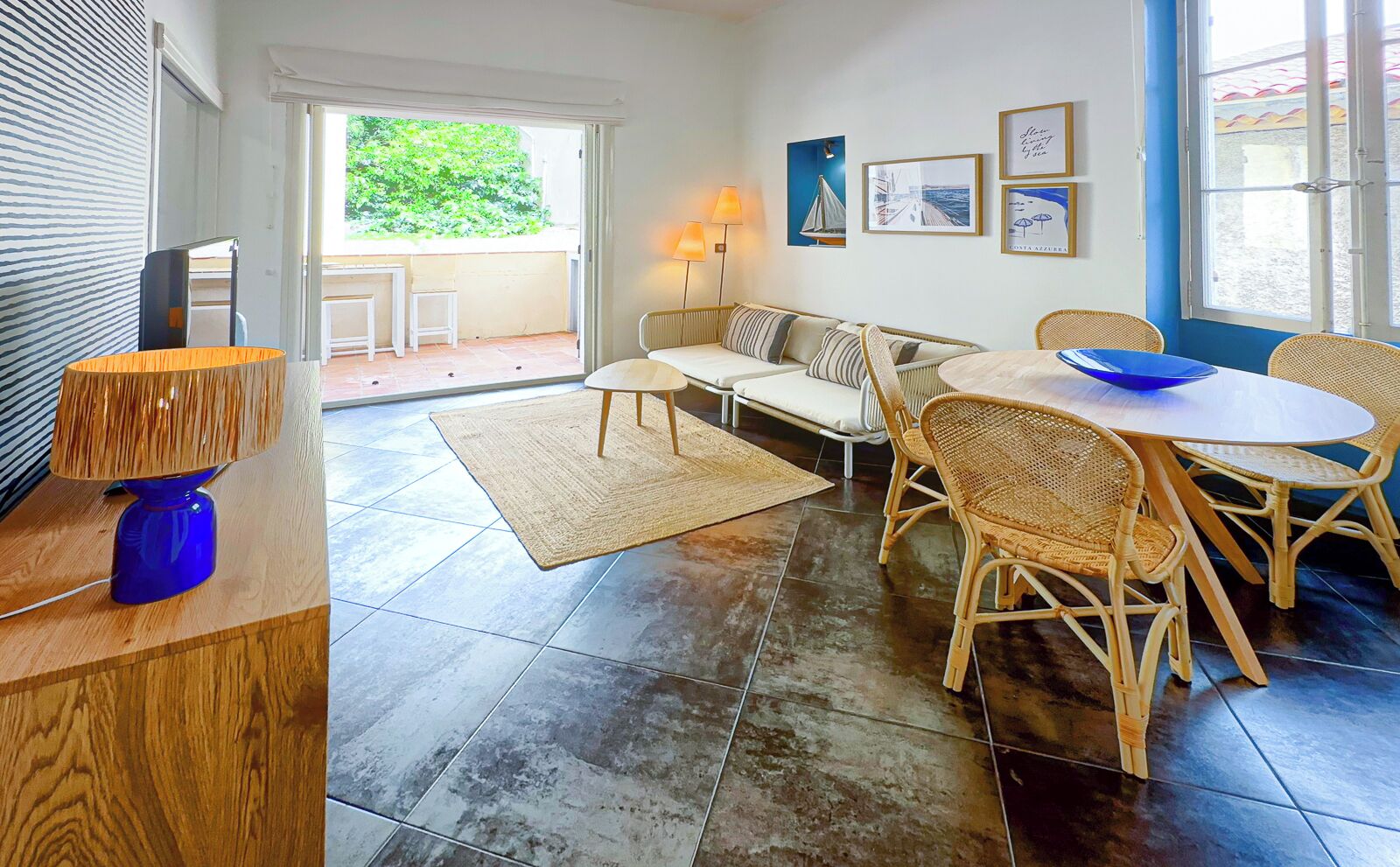 Un vaste espace de vie comprenant un canapé, une table basse, des fauteuils en osier, une table à manger et une lampe bleue.