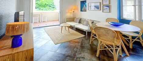 Un vaste espace de vie comprenant un canapé, une table basse, des fauteuils en osier, une table à manger et une lampe bleue.