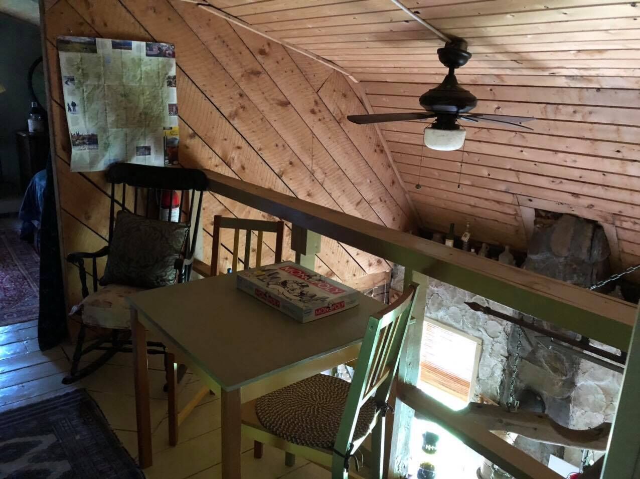 Ein rustikales Blockhaus-Interieur mit Holzbalkendecke, einem Tisch mit einem Gesellschaftsspiel, einem Stuhl und einem Kamin aus Stein.