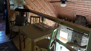 A rustic cabin interior with a wooden ceiling, a table with a board game, a chair, and a stone fireplace. - Delightful cordwood cabin -Westmore near Burke Mtn, Lake Willoughby - Jay Peak. (Westmore)