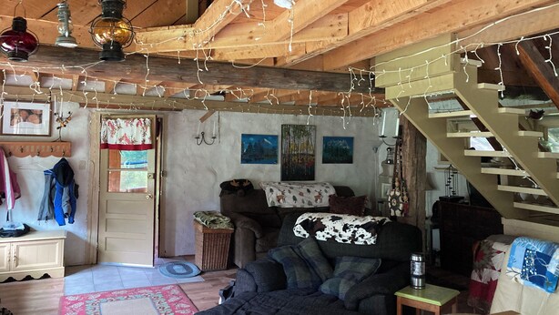 A cozy cabin interior with a wooden ceiling, a sofa, a small table, and a staircase. - Delightful cordwood cabin -Westmore near Burke Mtn, Lake Willoughby - Jay Peak. (Westmore)