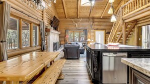 Ein Holzblockhaus-Interieur mit einem Holzesstisch, Bänken, einem Kamin, einer Couch und einer Küchenzeile inklusive Geschirrspüler.