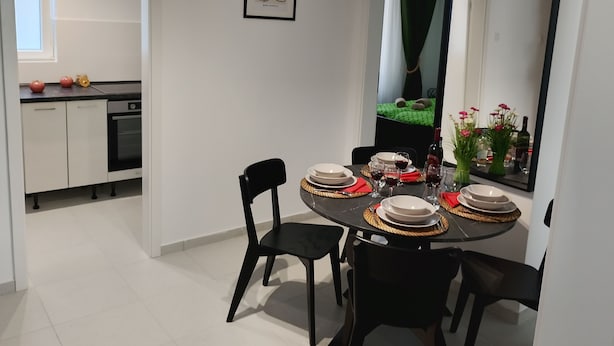 A dining area with a round table set for four, black chairs, and a large mirror reflecting the room.