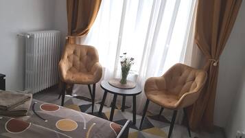 A room with a bed, two armchairs, a small table, a radiator, and a window with curtains.