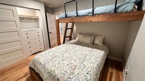A bunk bed with a floral bedspread, wooden flooring, and a white wardrobe with multiple drawers.