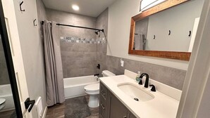 A modern bathroom with a bathtub, toilet, and vanity with a sink and mirror.
